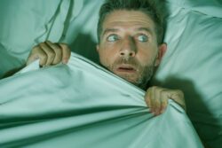 Man lying in bed, wearing frightened expression